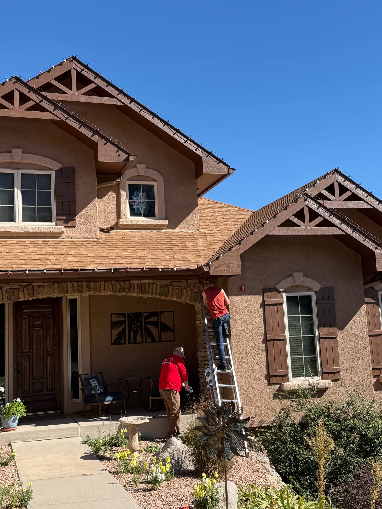 Front Range company crew on ladder installing roofline Christmas lights by the front porch Front Range company crew on ladder installing roofline Christmas lights by the front porch