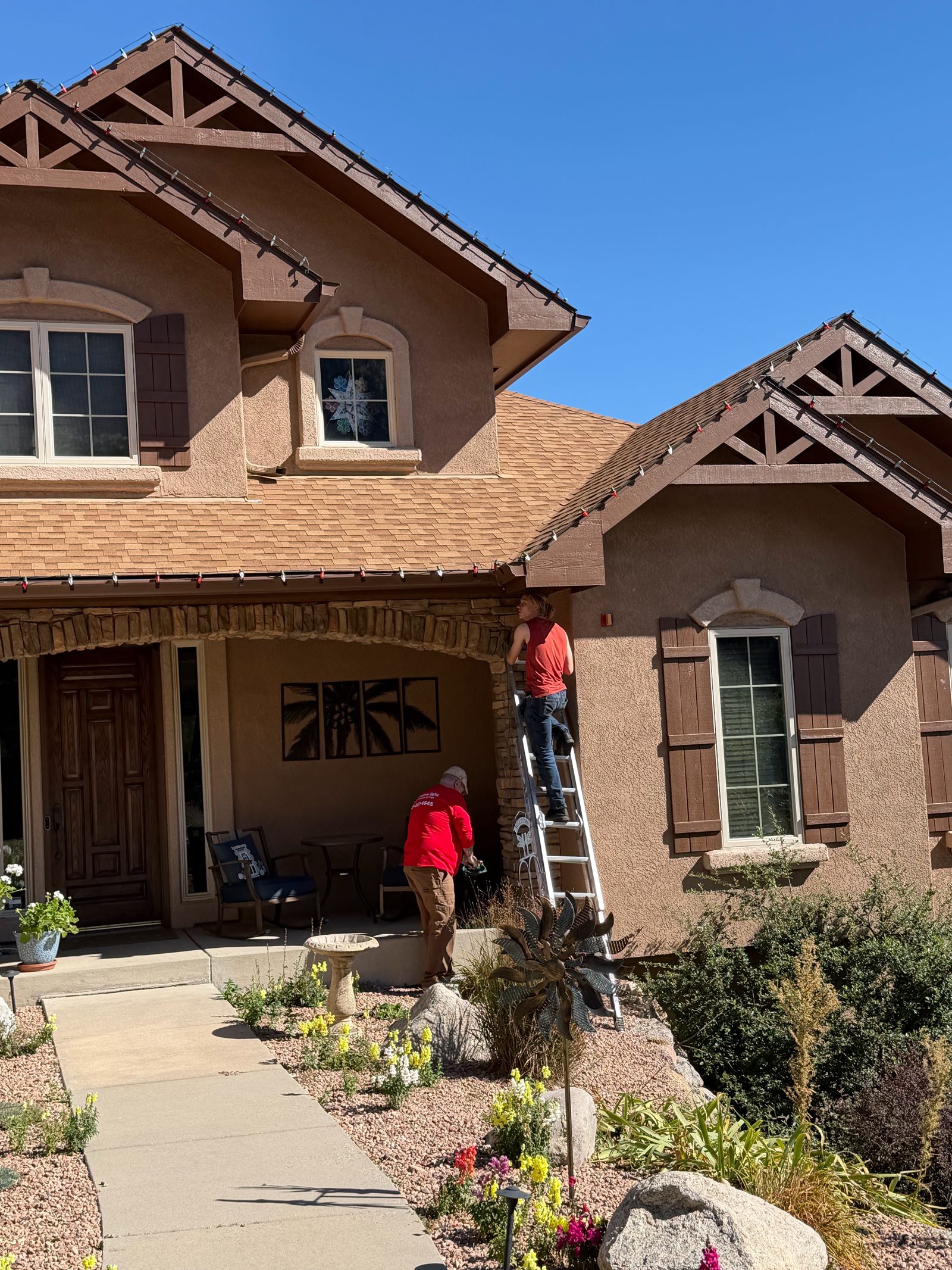 Christmas light installers on ladder hanging red Christmas lights on a Front Range home Christmas light installers on ladder hanging red Christmas lights on a Front Range home